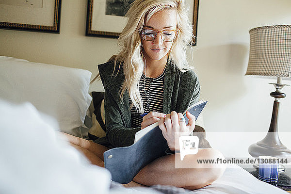 Frau schreibt Tagebuch  während sie zu Hause auf dem Bett sitzt