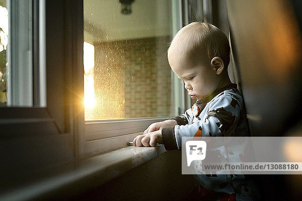 Kleiner Junge mit Mobiltelefon  der zu Hause am Fenster steht