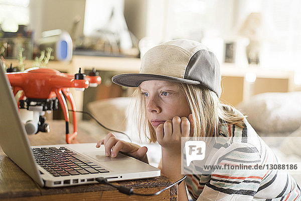 Boy working on laptop computer by drone at home