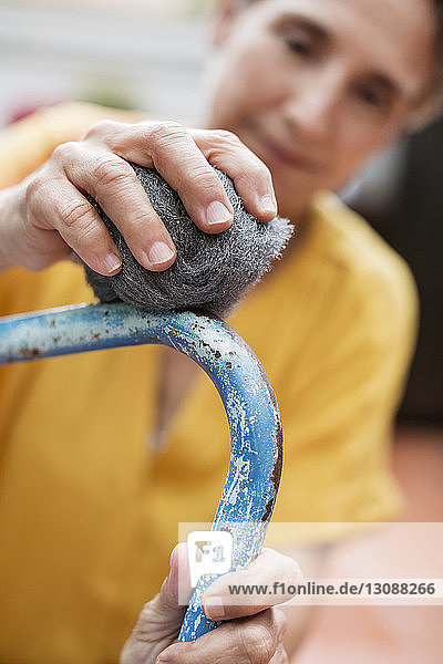 Close-up of mature woman scrubbing metallic chair with steel wool at yard