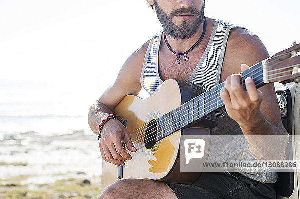 Midsection of man playing guitar while sitting on off-road vehicle during sunny day