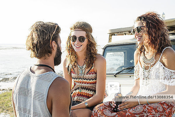 Man talking to female friends enjoying beer while sitting on off-road vehicle