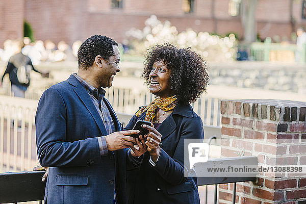 Glückliches Paar mit Mobiltelefon  das sich am Geländer in der Stadt anschaut