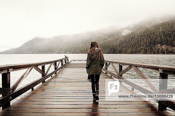 Rear view of woman walking on boardwalk at lake in foggy weather