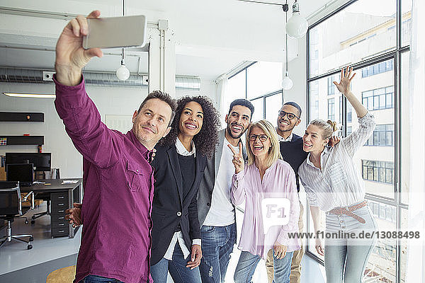 Happy business people taking selfie while standing by window in office
