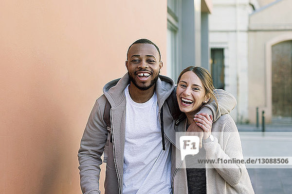 Portrait of cheerful man standing with arm around woman on street