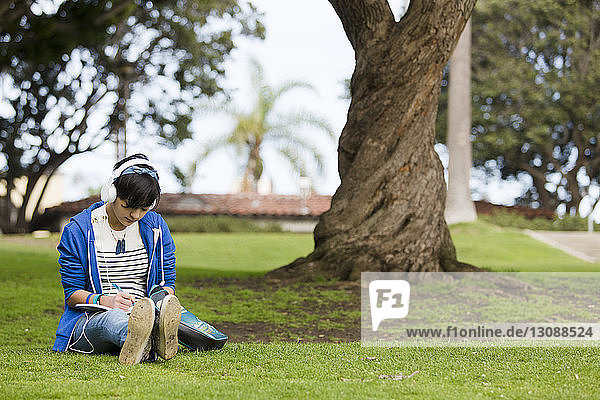 Teenager-Mädchen schreibt auf Tagebuch  während sie im Park Musik hört