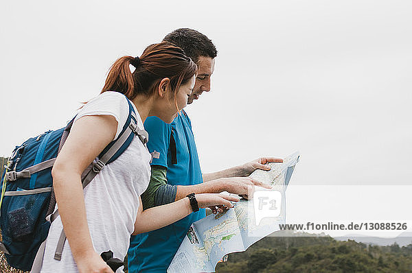 Friends analyzing map while standing against clear sky