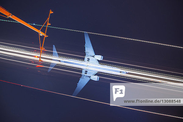 Niedrigwinkelansicht des Signalmastes gegen Lichtspuren und Flugzeug am nächtlichen Himmel