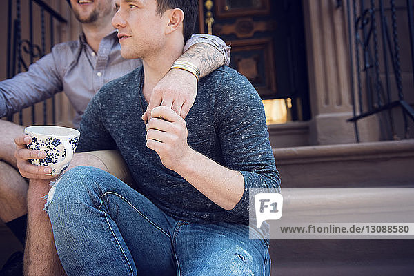 Midsection of gay couple sitting on steps outside house
