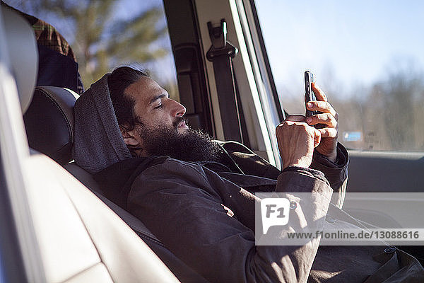 Seitenansicht eines Mannes  der ein Smartphone benutzt  während er im Auto sitzt