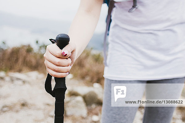 Midsection of female hiker holding hiking pole while standing on mountain