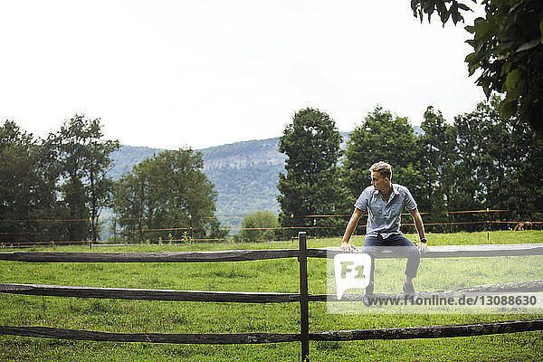 Mann sitzt auf Holzzaun gegen klaren Himmel auf Bauernhof