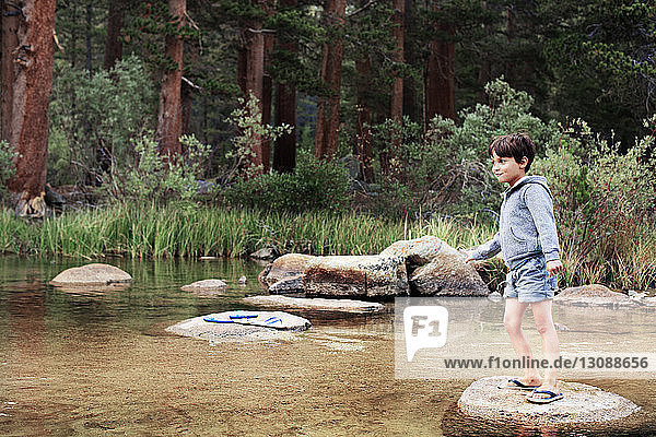 Happy boy standing on rock at stream against trees
