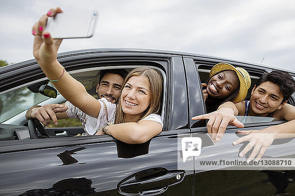 Happy male and female friends taking selfie while sitting in car