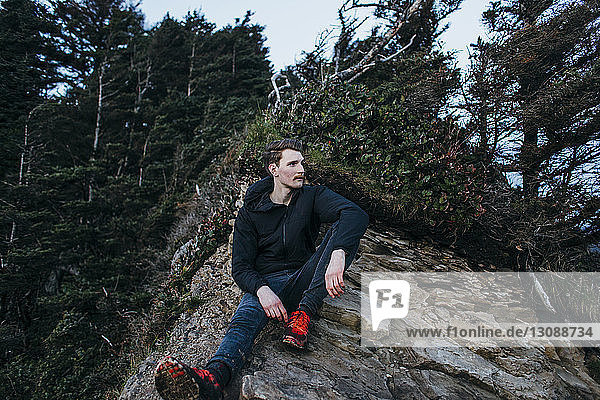 Nachdenklicher männlicher Wanderer sitzt auf Fels gegen Bäume