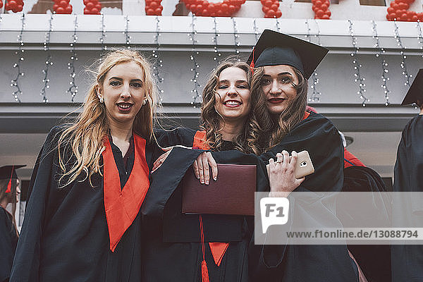 Porträt von glücklichen Studentinnen in Graduationskleidern gegen Gebäude