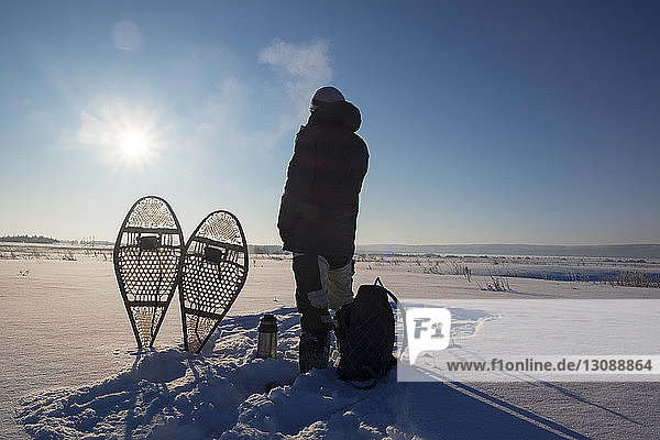 Rückansicht eines Mannes  der an einem sonnigen Tag auf einem schneebedeckten Feld gegen den Himmel steht