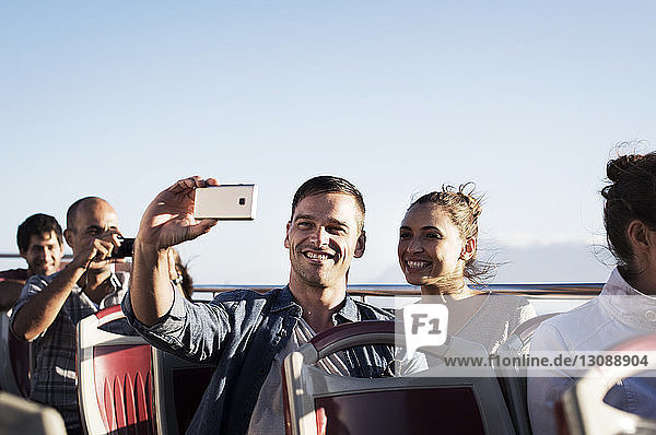 Couple taking selfie while traveling in double-decker bus against clear sky
