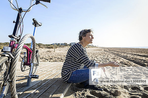 Nachdenkliche Frau spielt mit Sand  während sie mit dem Fahrrad am Strand sitzt
