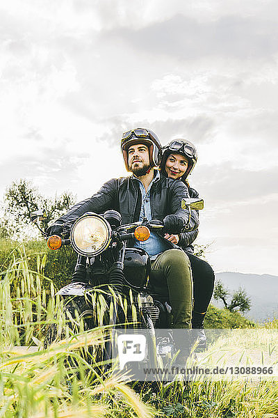 Ehepaar schaut weg  während es auf einem Motorrad gegen den Himmel sitzt