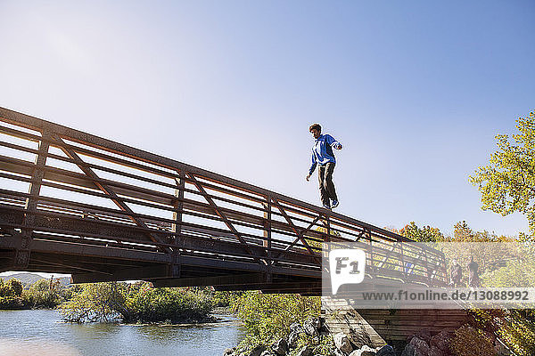 Niedrigwinkelansicht eines Mannes  der auf dem Brückengeländer vor klarem blauen Himmel geht
