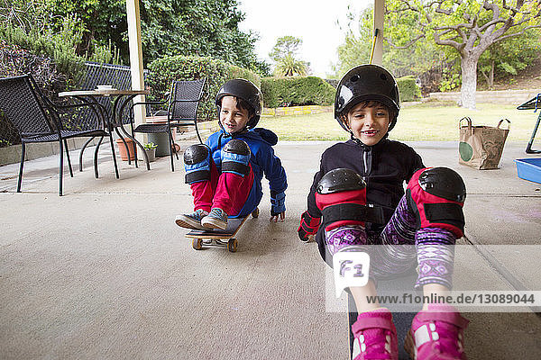 Happy siblings sitting on skateboards at yard