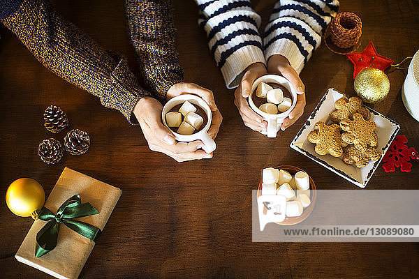 Ausgeschnittenes Bild eines Paares  das Marshmallow-Kaffee mit Keksen bei Tisch trinkt