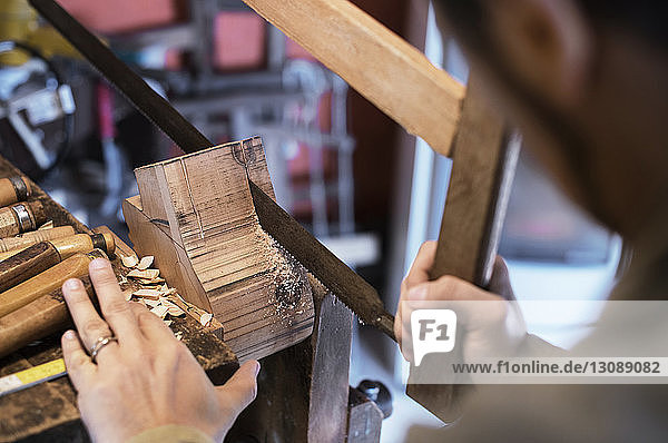 Beschnittenes Bild eines Mannes  der in einer Werkstatt mit einer Handsäge Holz schneidet
