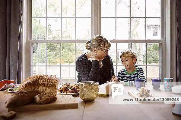 Mutter spricht mit Sohn während des Essens am Tisch gegen das Fenster im Wohnzimmer