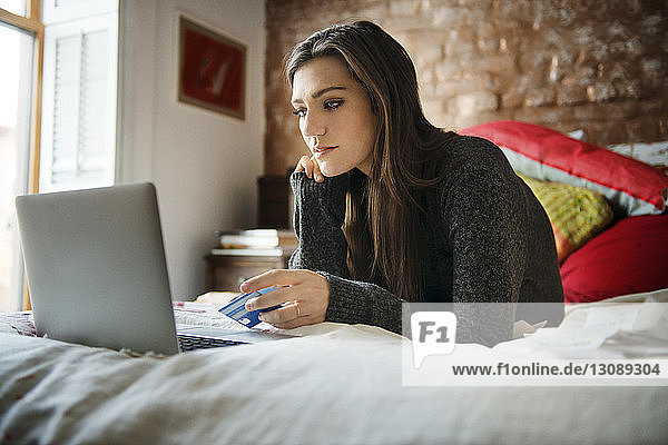 Woman shopping online on laptop while lying on bed at home