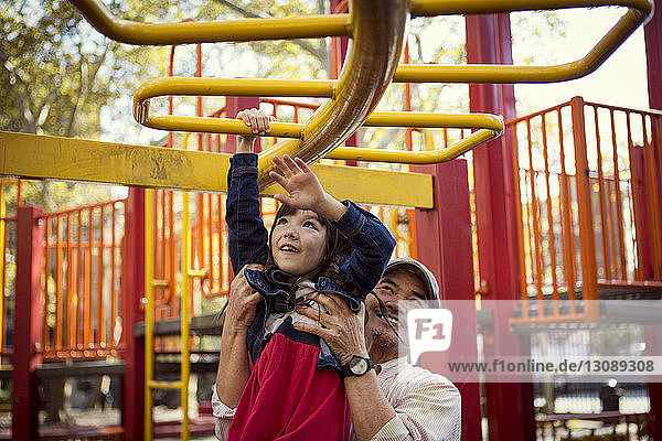 Grandfather assisting granddaughter for hanging on jungle gym