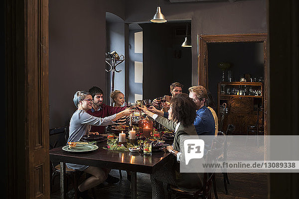 Friends toasting wine while having meal at table during Christmas