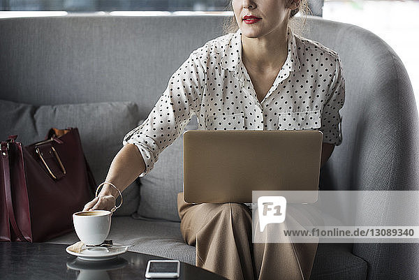 Businesswoman holding coffee cup while working on laptop at restaurant