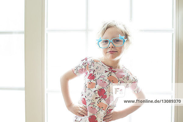 Portrait of girl wearing eyeglasses standing by window at home