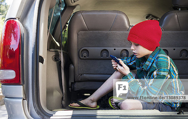 Boy using mobile phone while sitting in back of car