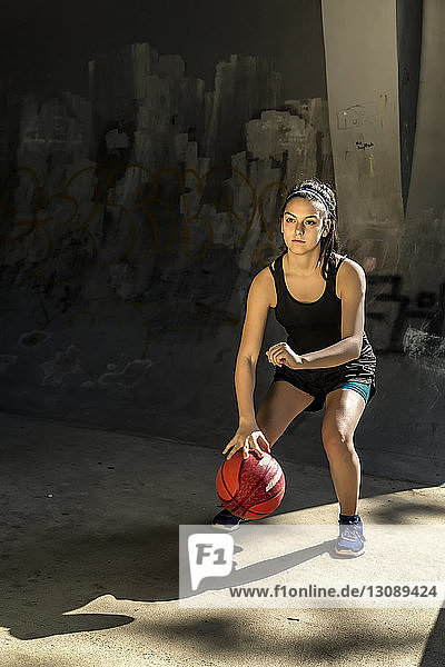 Portrait of confident athlete playing basketball against wall