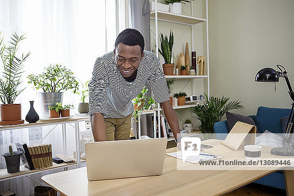 Glücklicher Mann mit Laptop am Tisch im Heimbüro
