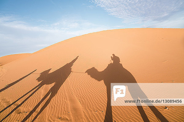 Schatten von Freunden reitet Kamele auf Sand in der Wüste Merzouga gegen den Himmel