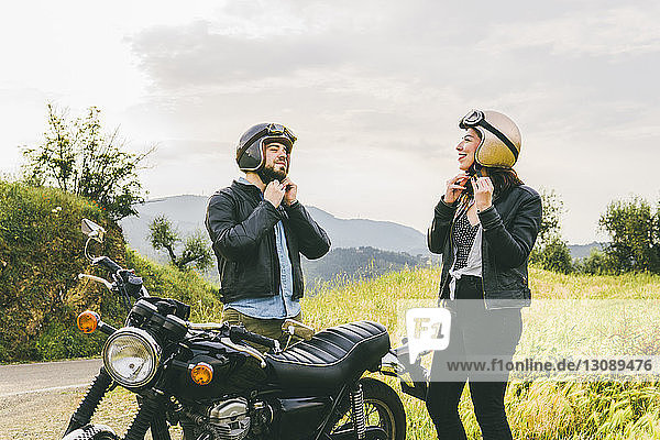 Paar trägt Helme  während es mit dem Motorrad gegen den Himmel steht