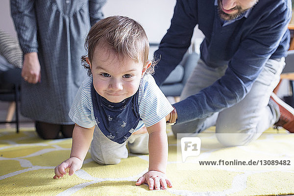 Glückliche Eltern sehen ihren Sohn zu Hause auf dem Teppich krabbeln