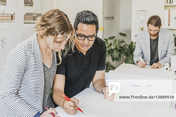 Colleagues discussing while man writing in office