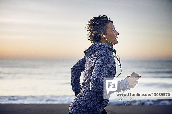 Woman jogging while listening music at beach against sky