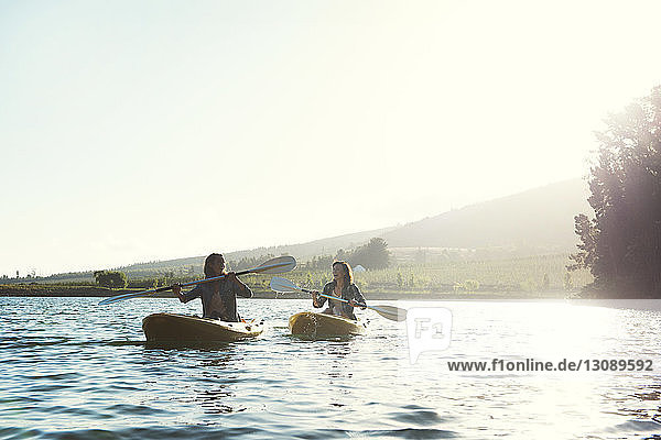 Cheerful female friends kayaking on lake clear sky during sunny day