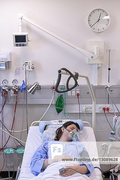 High angle view of female patient wearing oxygen mask while resting on bed in hospital