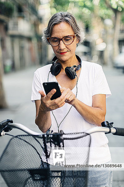 Frau benutzt Smartphone  während sie mit dem Fahrrad auf der Straße steht