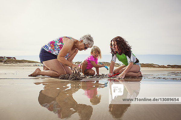 Enkelinnen mit Großmutter graben kniend im Sand am Strand