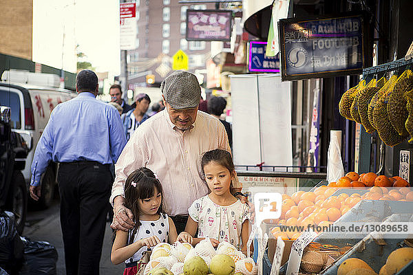 Großvater mit Enkelinnen am Obststand auf dem Markt
