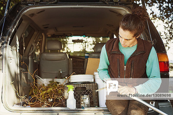Frau untersucht Gartengerät  während sie im Kofferraum eines Autos sitzt