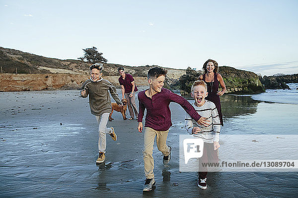 Verspielte Brüder laufen am Strand mit Eltern und Hund im Hintergrund